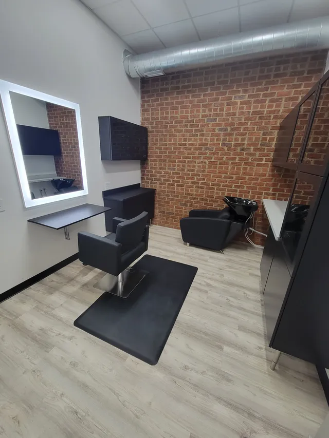 An interior suite with exposed brick, styling chair, shampoo bowl, and lit mirror