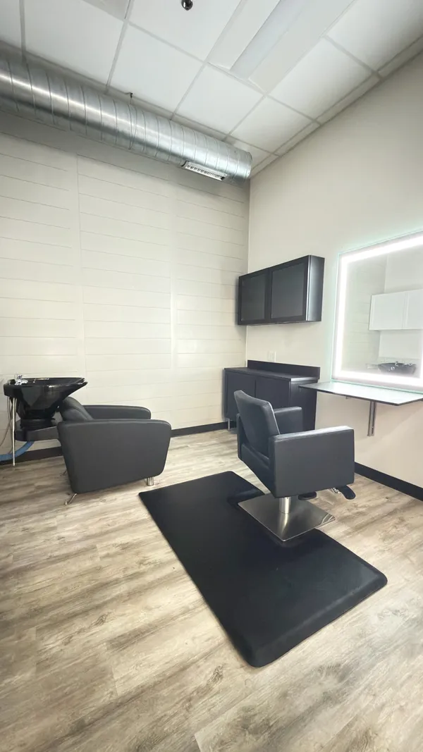 An interior suite with shiplap walls, styling chair, shampoo bowl, and lit mirror