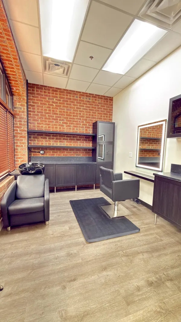A window suite with exposed brick, styling chair, shampoo bowl, and lit mirror