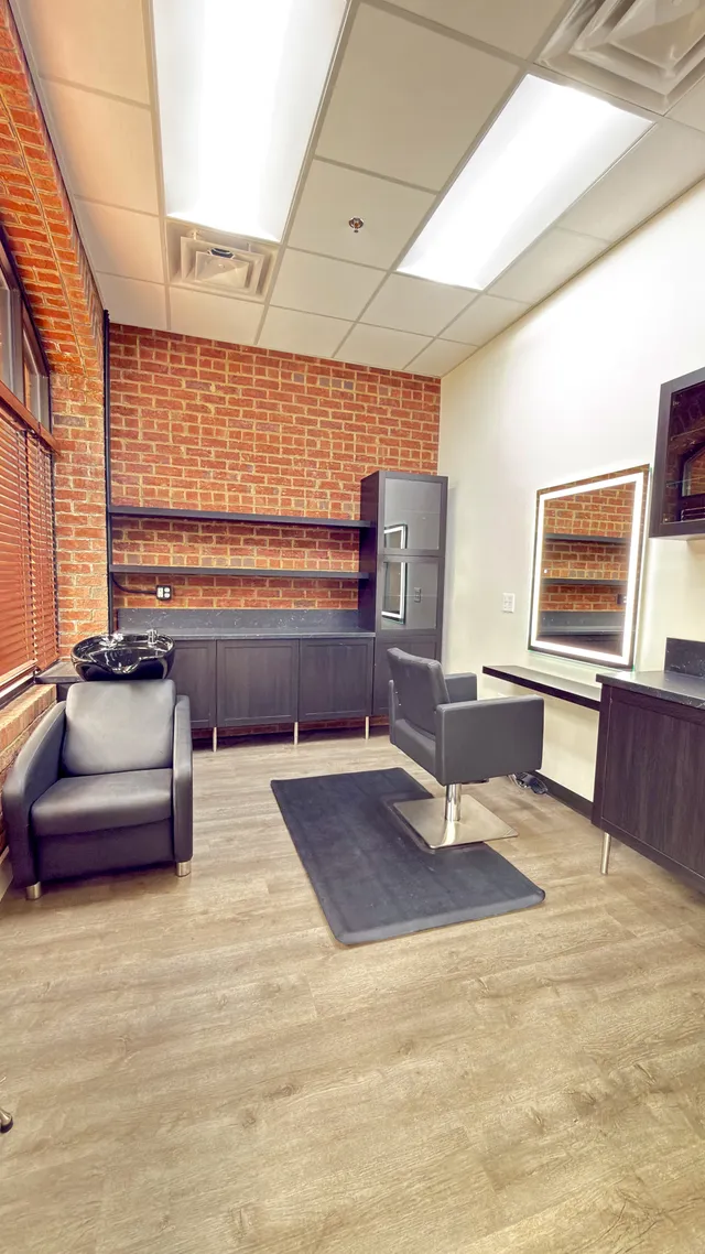A window suite with exposed brick, styling chair, shampoo bowl, and lit mirror